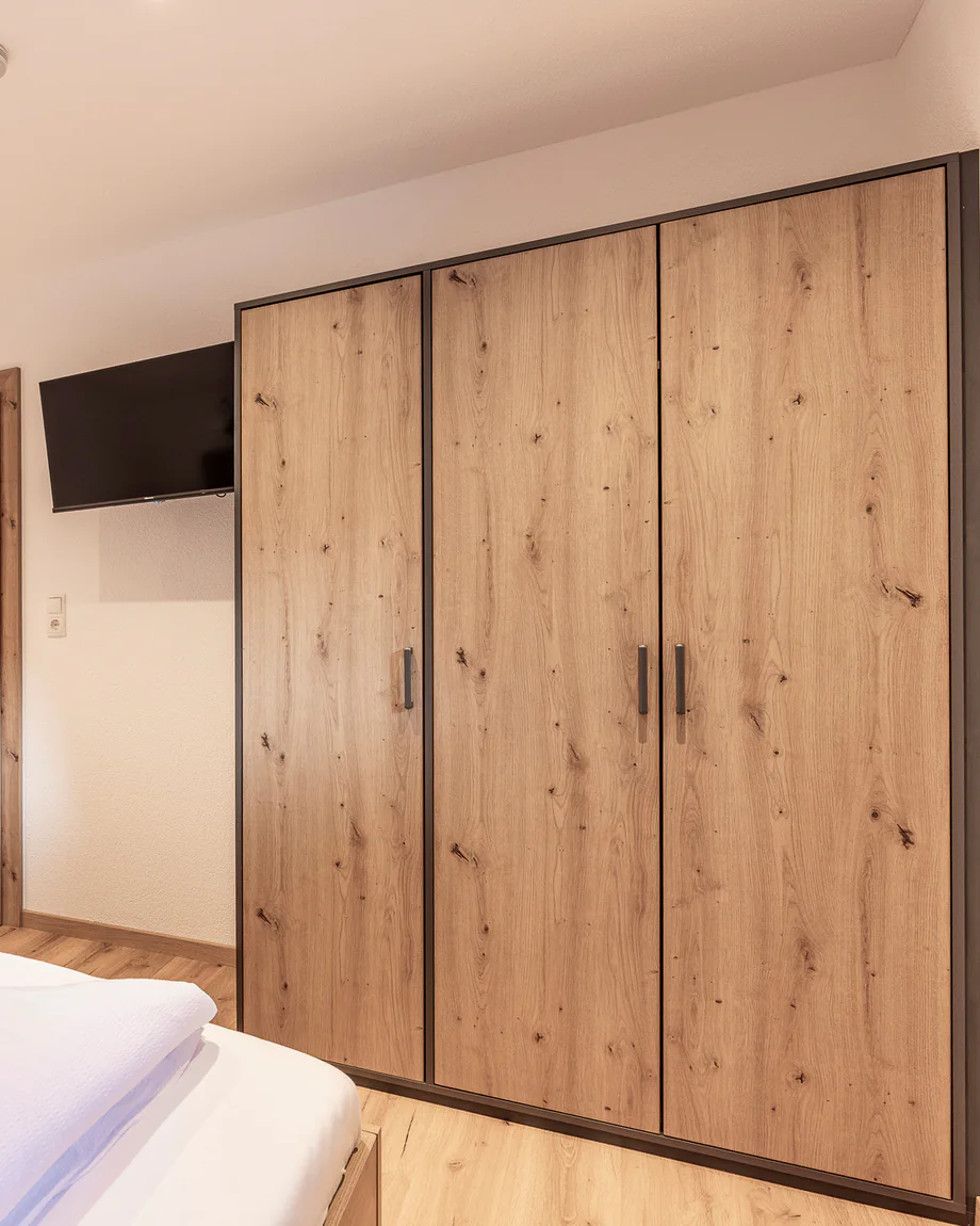 Großer dreitüriger Kleiderschrank, daneben ein Flat-TV an der Wand