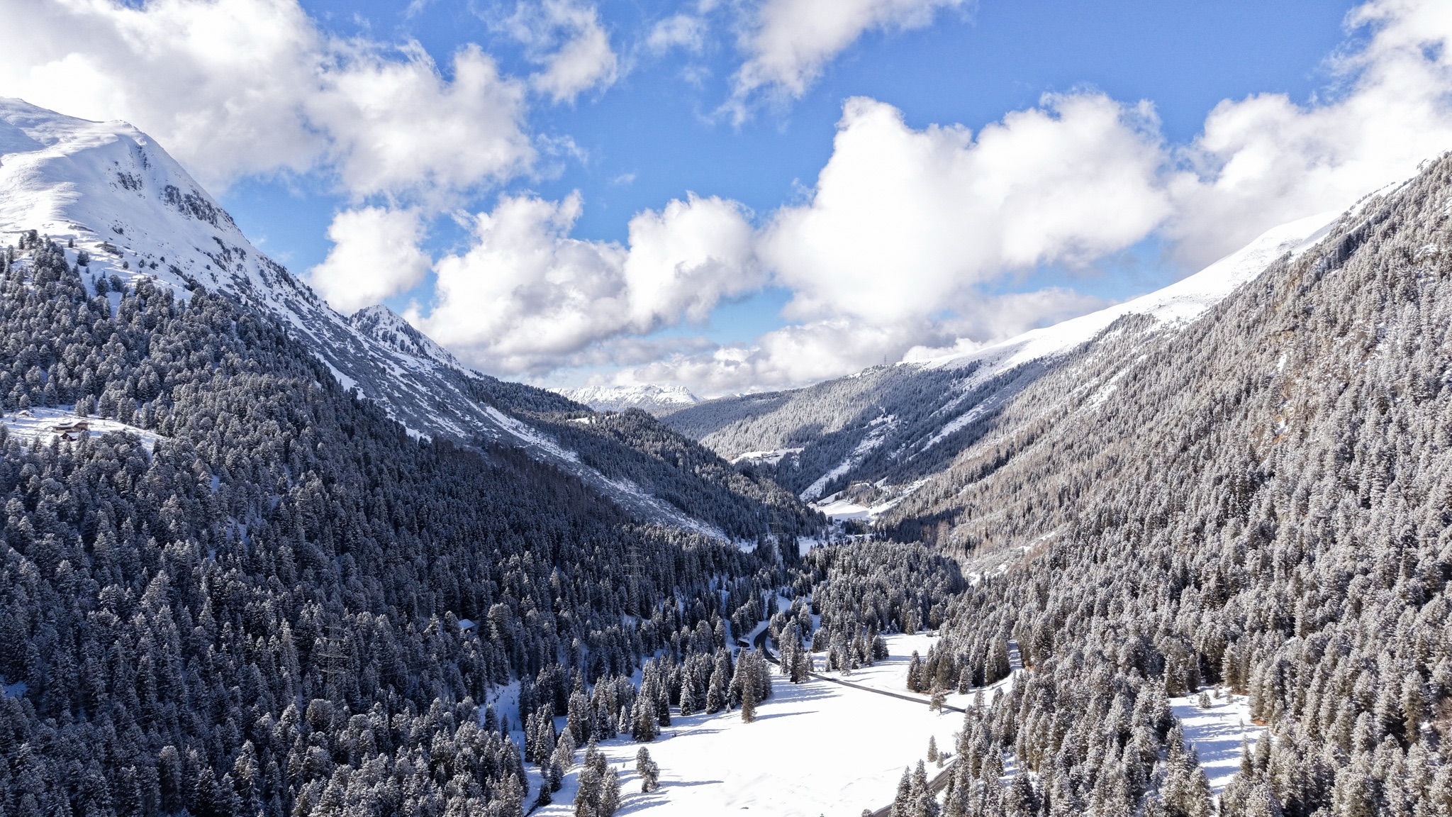 Verschneites Bergtal mit Tannen und Gipfeln, von oben gesehen